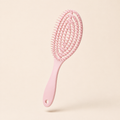 Glidura scalp massage brush in pink, angled view on an ivory background